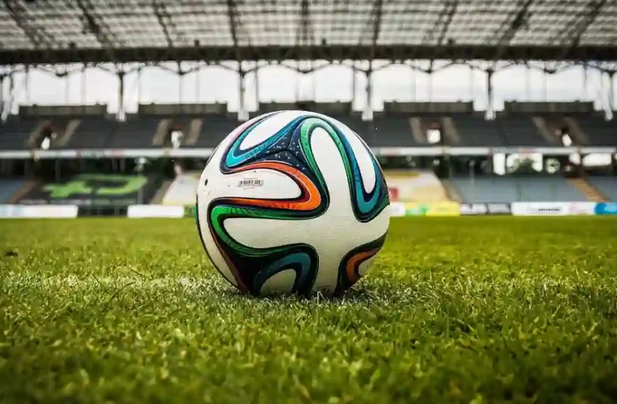 A leather football nestled in the center circle of a sun-drenched, empty football field