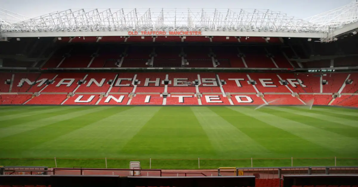 An empty football ground with red seats, featuring the visible name 'Old Trafford Manchester' and 'Manchester United' written on the chairs.