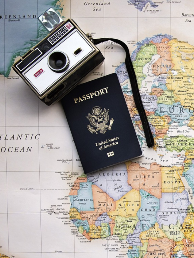 A camera and passport placed on a paper world map.