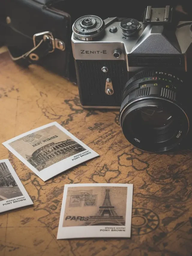 An overhead view of a world map with a camera placed on top. Three printed photographs lie beside the camera on the map